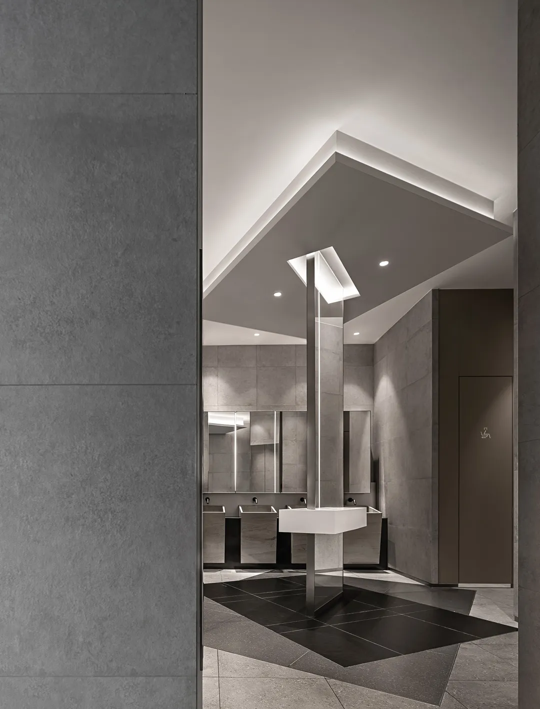 Modern public restroom with concrete walls and flooring, illuminated by recessed lighting.