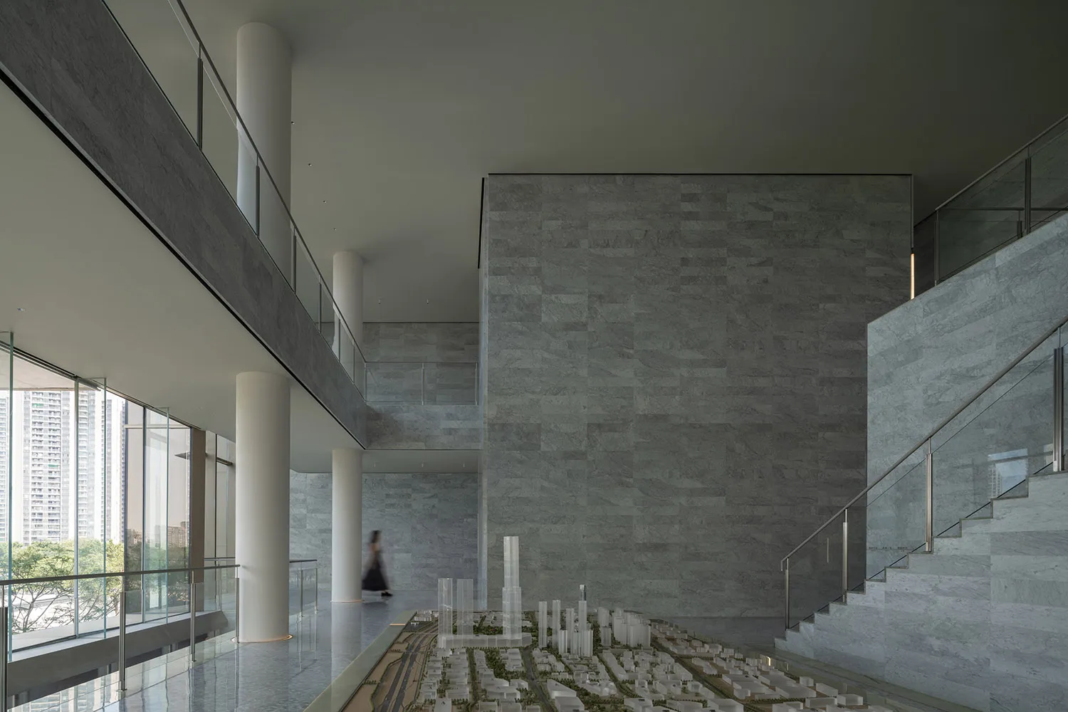 A modern interior space with concrete walls and flooring, featuring architectural models and high ceilings with large windows