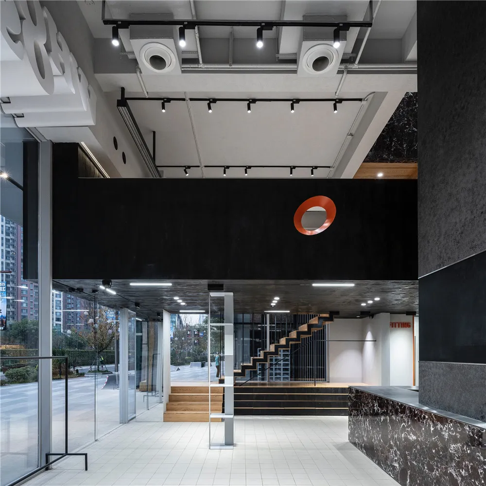 Modern office lobby with glass walls, minimalist lighting, and casual seating.