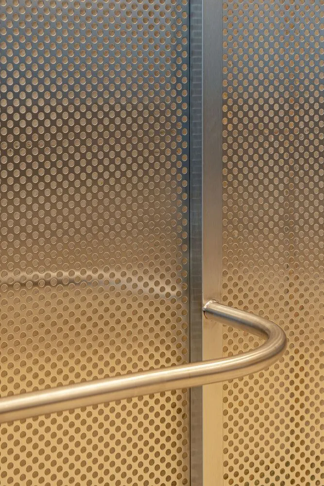A close-up of a metallic handle on a perforated metal wall in an industrial interior setting.