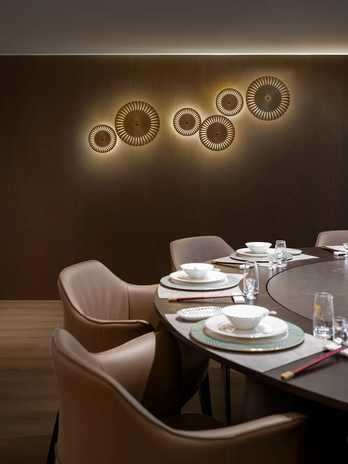 Modern dining room with round table and brown leather chairs, featuring wood and glass accents.