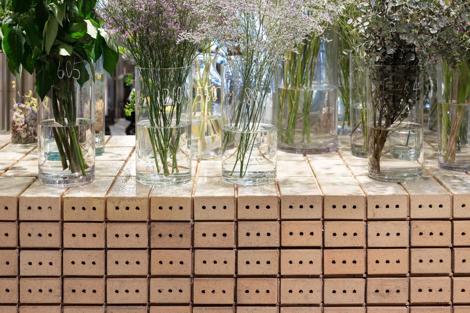 An arrangement of floral displays in clear glass vases on a brick platform.