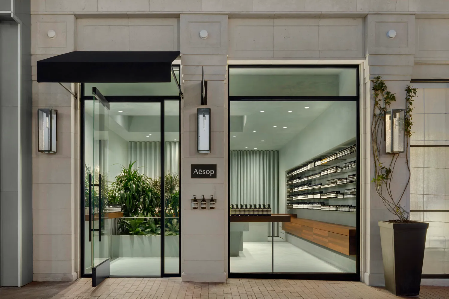 Storefront with glass panel, concrete column, and plants outside.