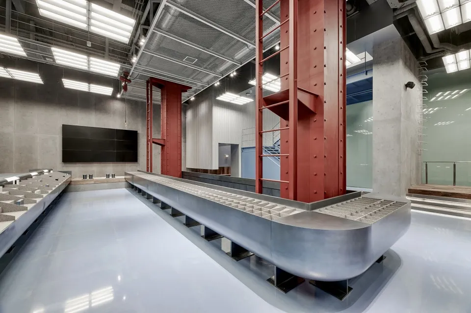 A modern laboratory with exposed concrete walls, a conveyor belt, and red structural columns.