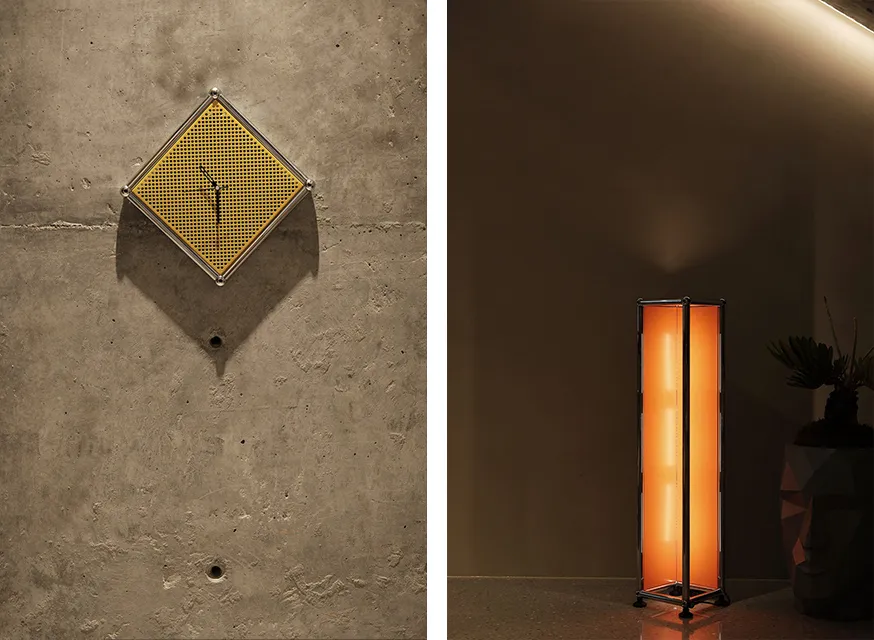 A square, modern pendant lamp with a perforated metal shade hangs from a concrete wall.