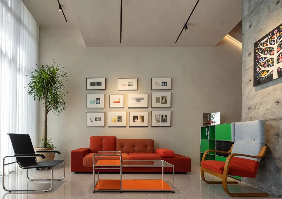 A modern living room with concrete walls, glass coffee tables, and a red sofa.