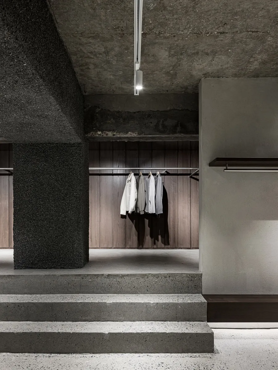 Modern clothing shop interior with concrete and wooden surfaces, featuring clothing racks.