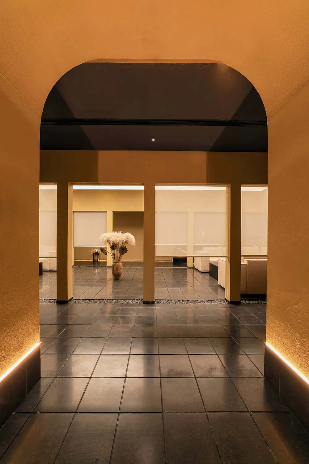A minimalist interior space with black tiles and concrete elements, featuring a vase of white flowers.