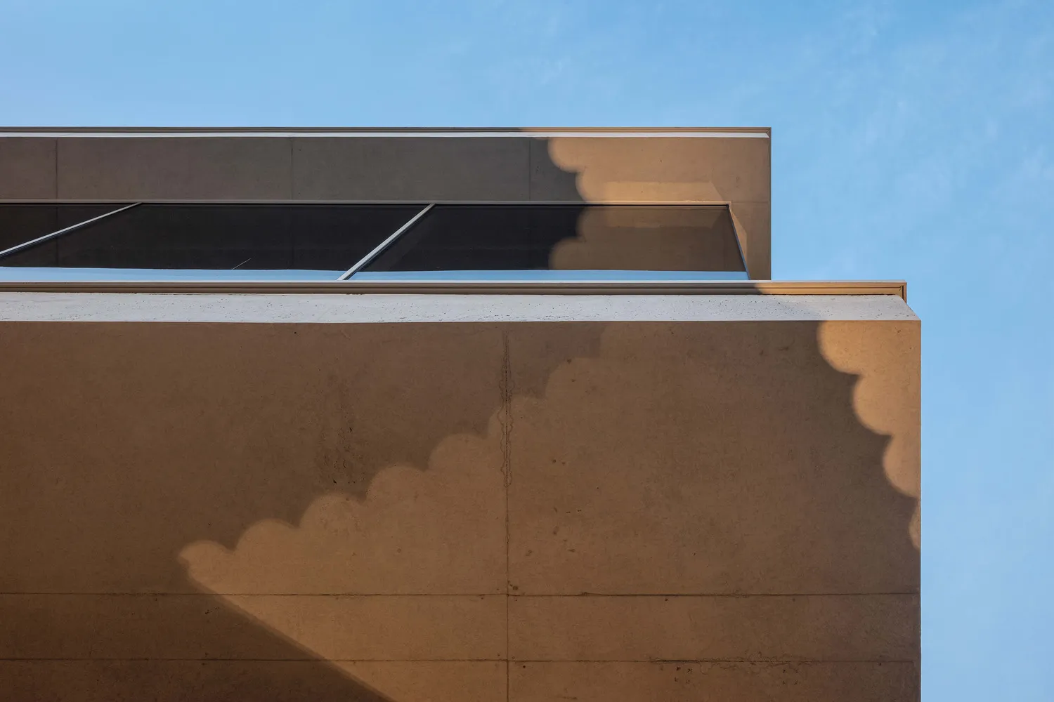 Modern building facade with concrete walls and geometric windows against a blue sky.