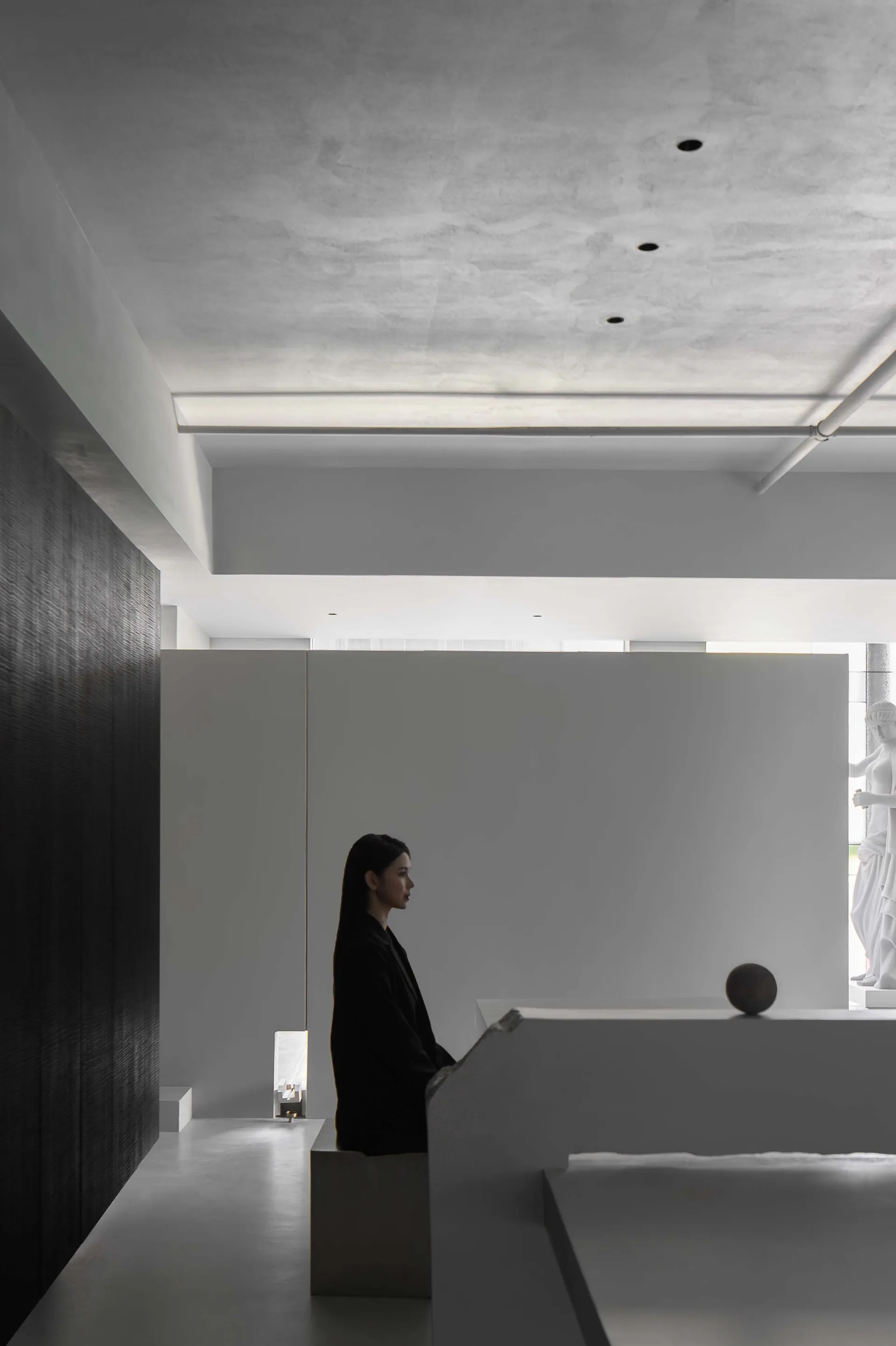 A minimalist space featuring exposed concrete walls and ceiling, with a lone figure standing in the background.
