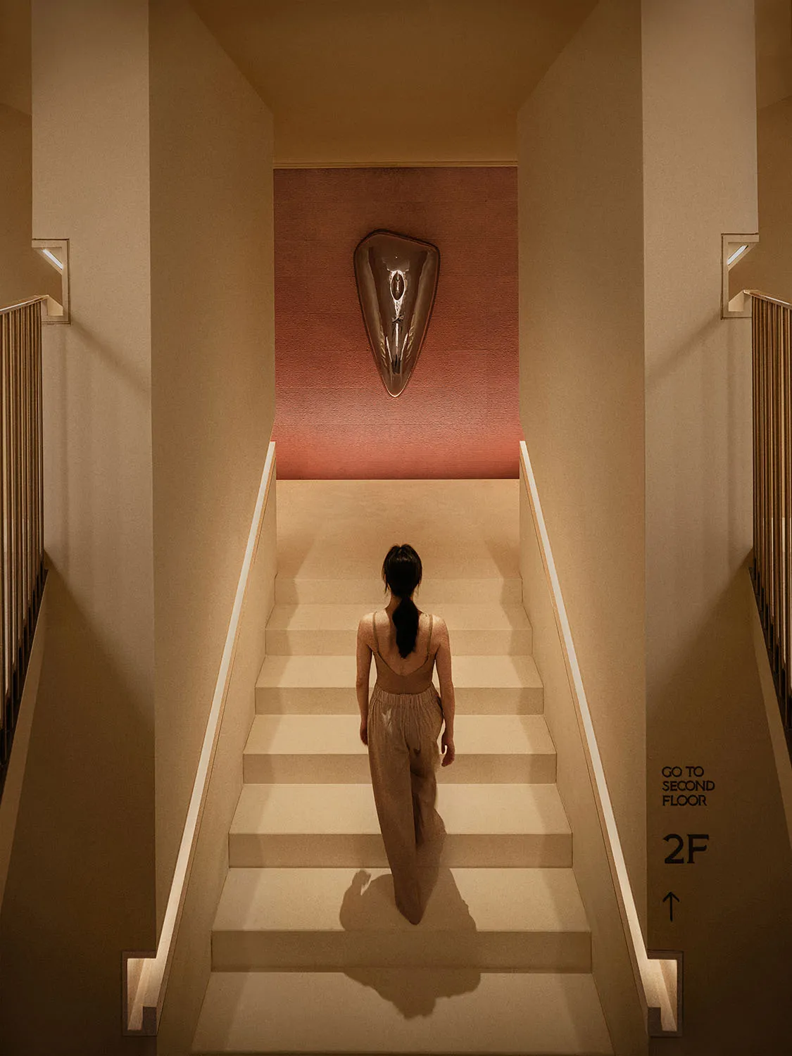 A woman walking up a white staircase with a metallic shield wall art above her.