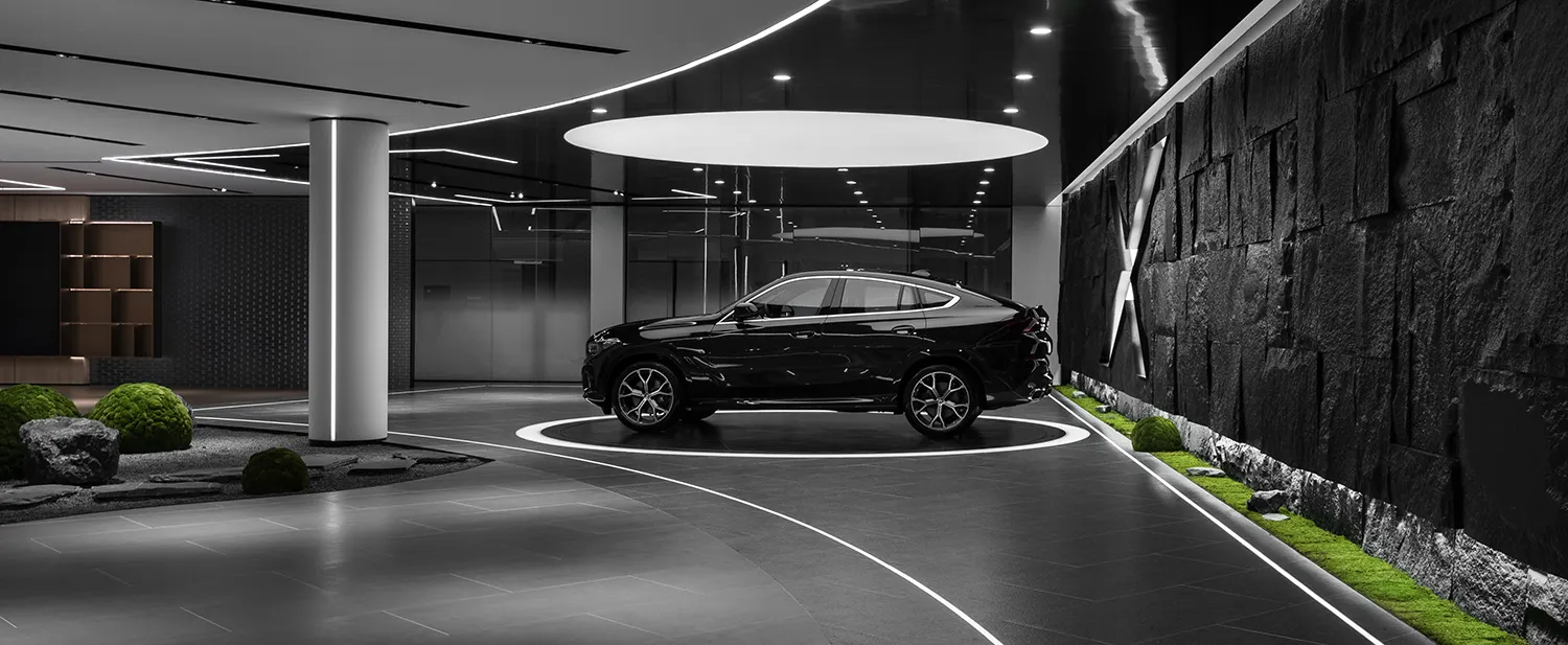 A black and white luxury car parked in a modern, minimalist lounge with concrete and glass materials