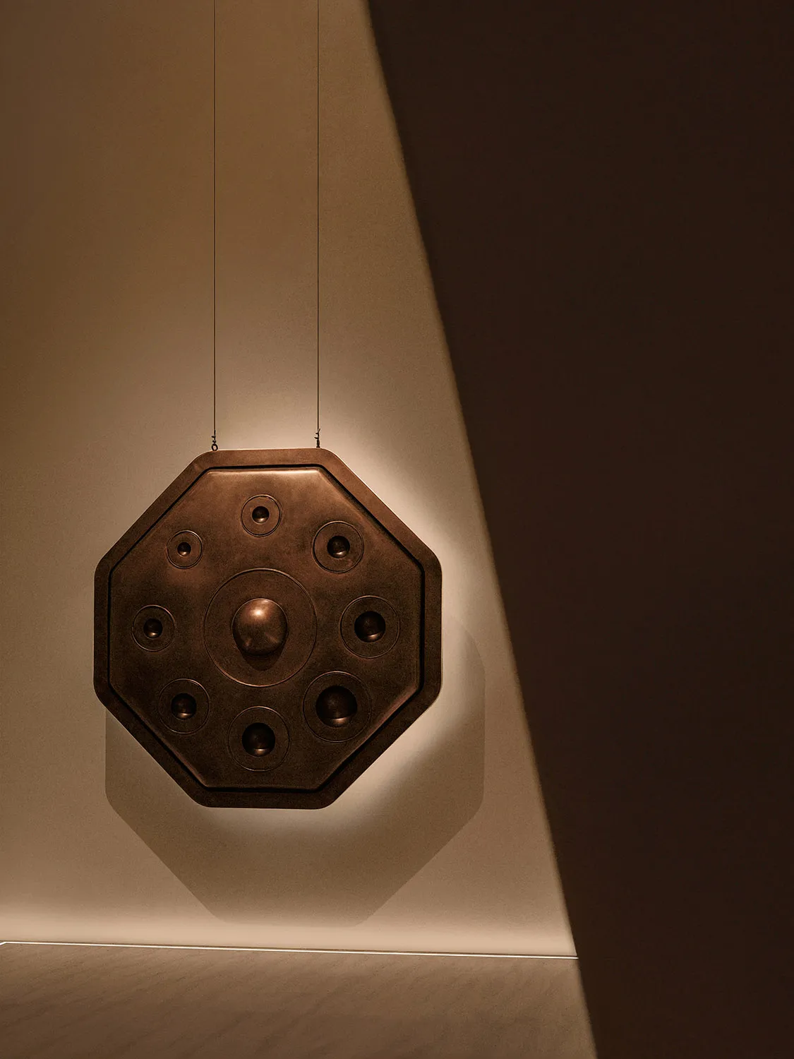 A minimalist metal decorative object with lighting features hanging in a neutral setting.