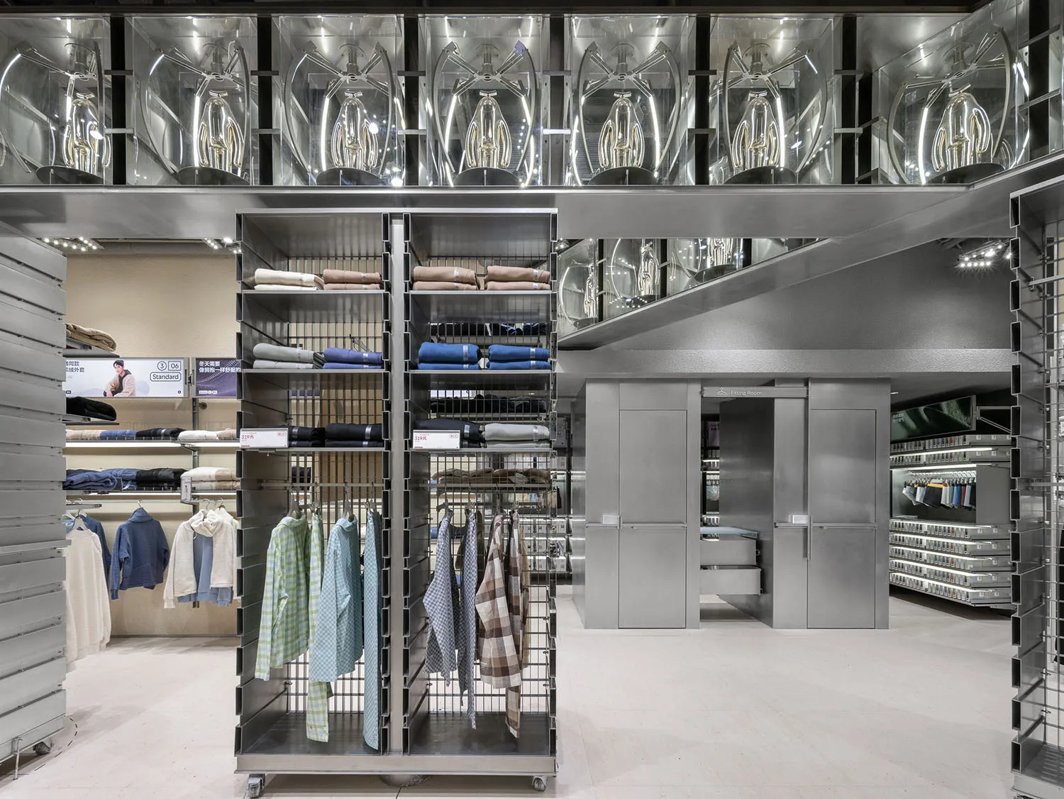 A commercial retail shop interior featuring metallic shelving units with clothing items and a glass ceiling with industrial l