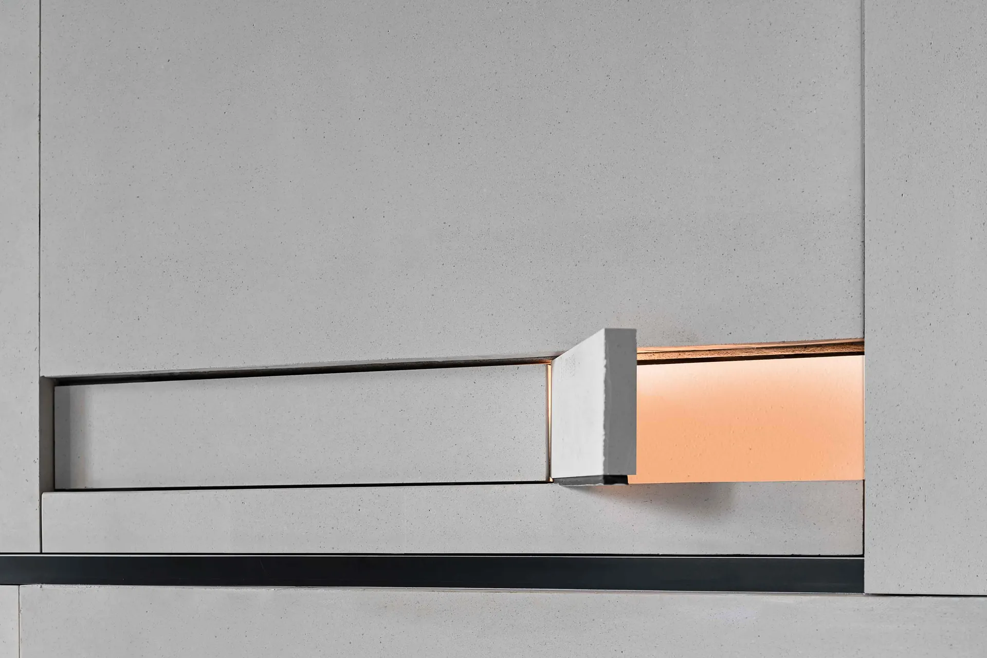 A minimalist interior design featuring a concrete wall with a recessed, illuminated lamp.
