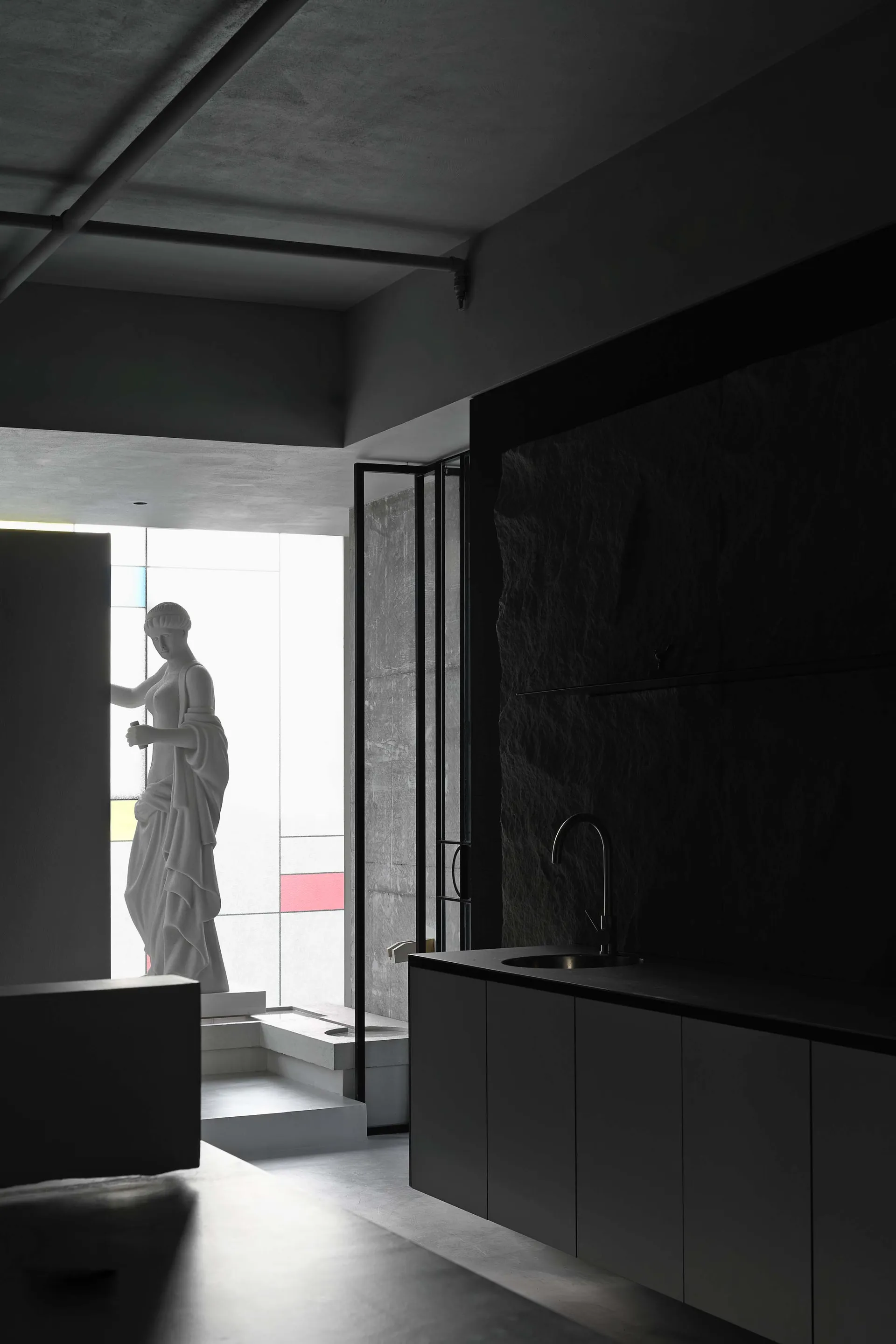 A minimalist modern kitchen featuring black marble countertops and concrete walls.