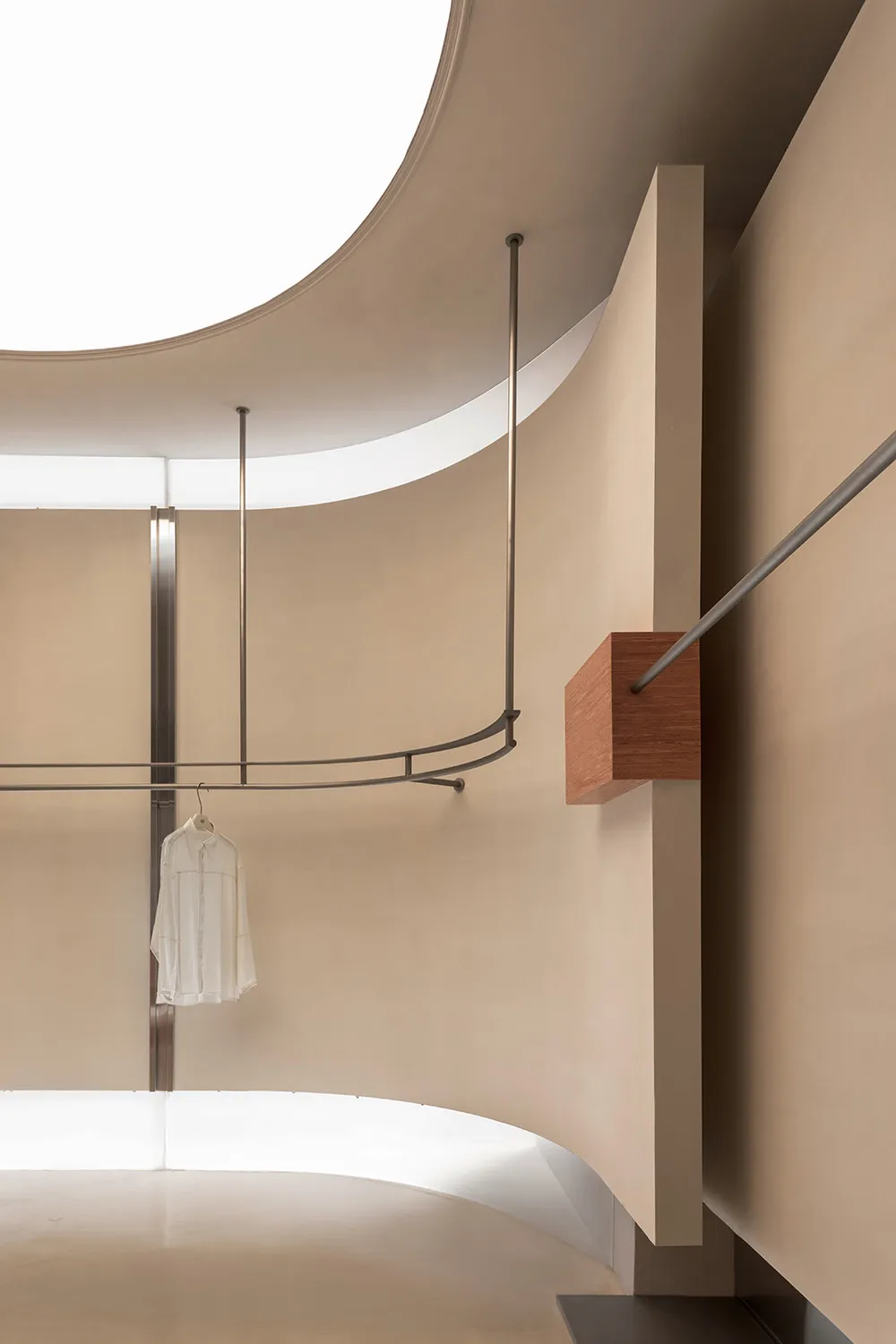 A minimalist clothing display featuring a white garment on a metal rod in a curved, nude-colored space.