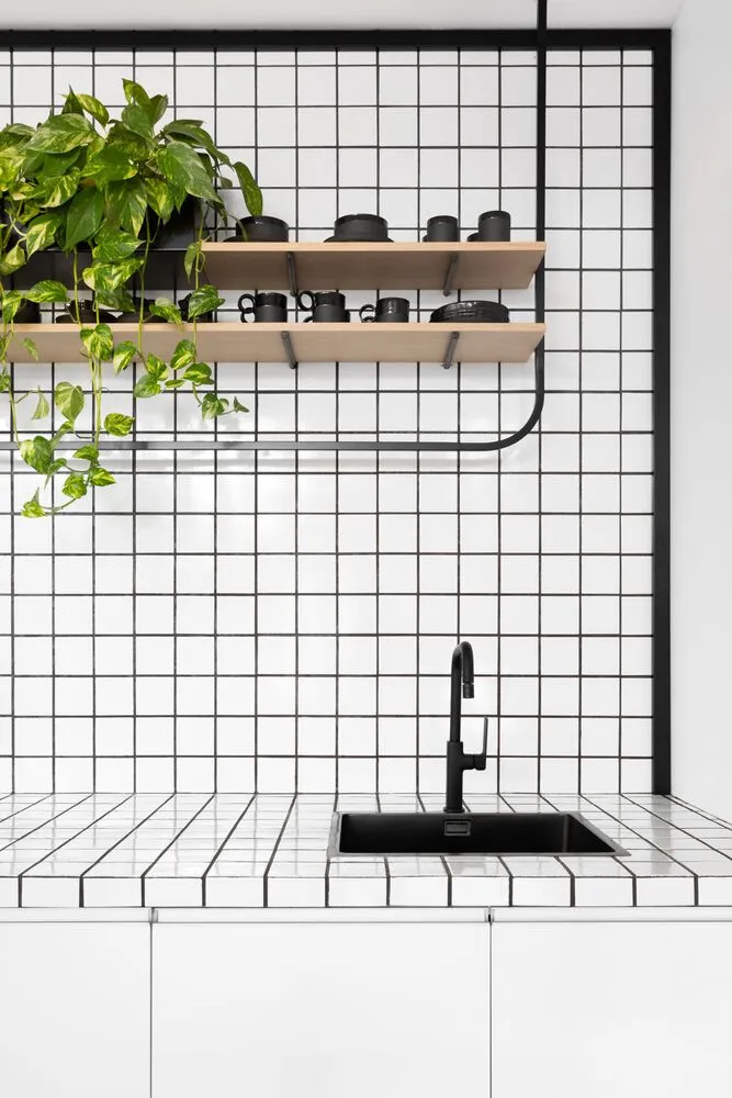 A modern minimalist kitchen with white tiled walls and black appliances and accessories.