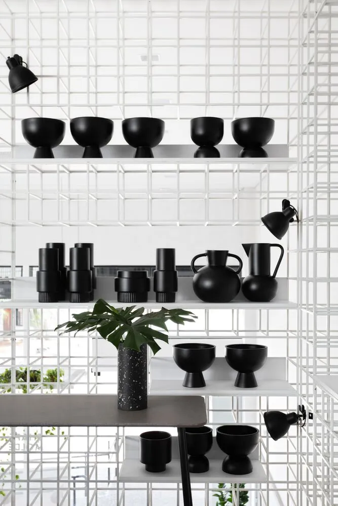Black ceramic vessels and bowls arranged on white shelves in a minimalist interior design setting.
