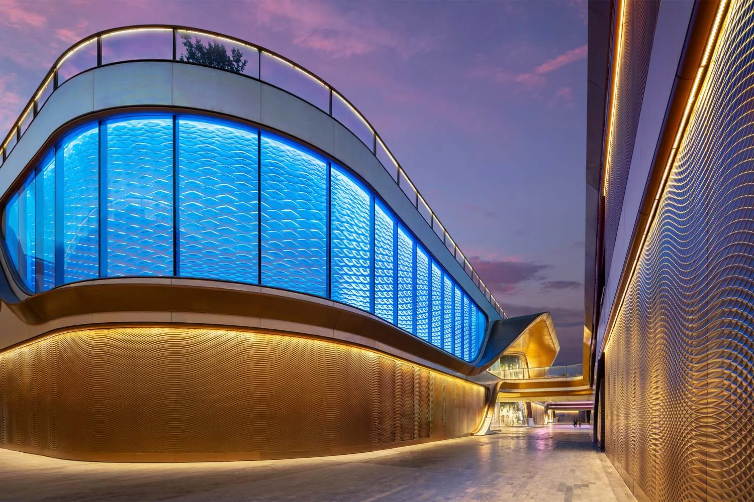 A modern retail pavilion with glass walls and blue lighting at dusk.