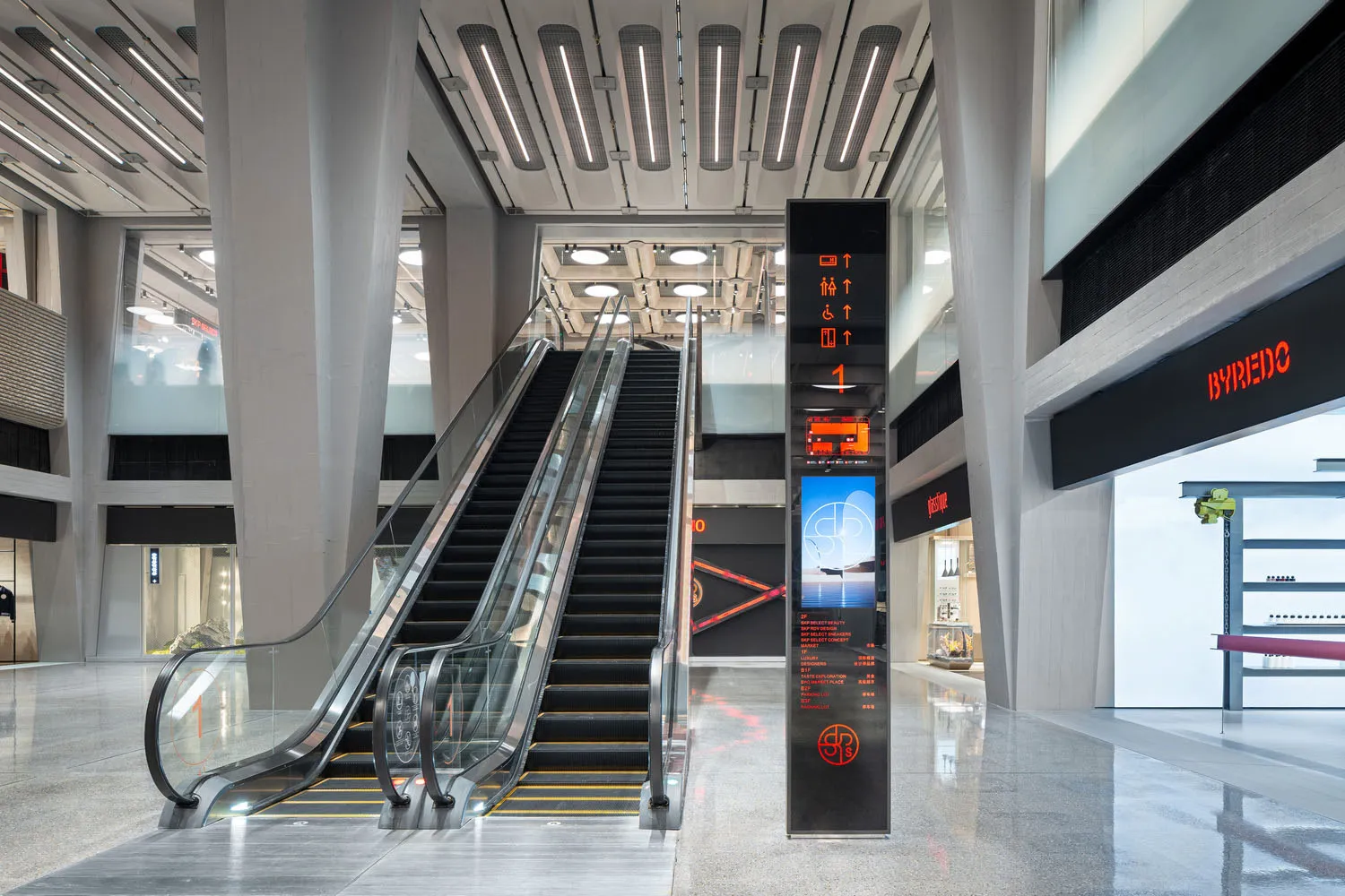 A modern shopping center with glass and concrete design, featuring escalators.