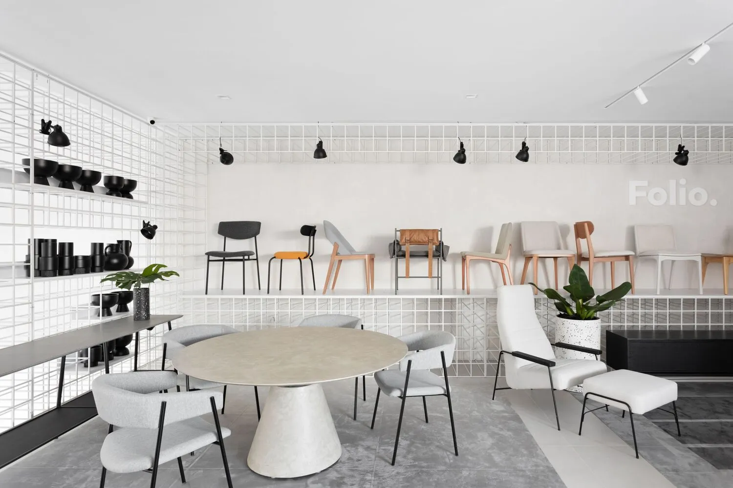 Modern showroom interior with metal shelving, fabric seating, wooden chairs, and concrete table