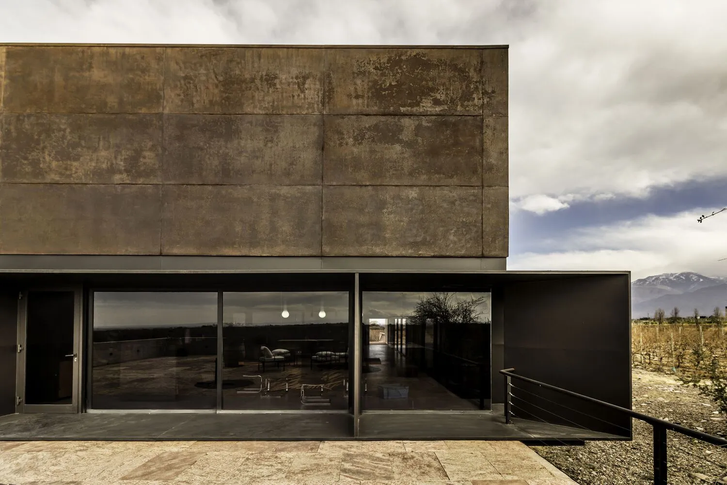 A modern metal-clad residential exterior with large glass windows reflecting the surrounding landscape.