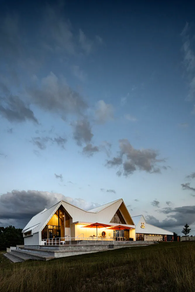 Modern commercial building with metal-clad angled roof, illuminated exterior at dusk with cloudy sky