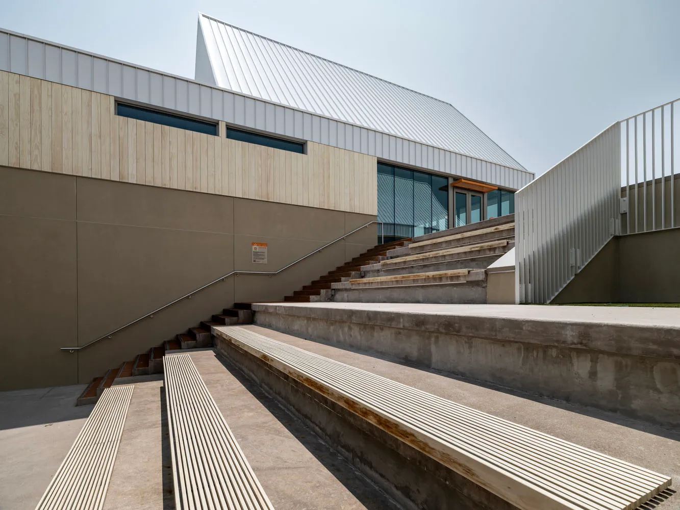 A modern architectural structure with metal roof, wooden elements, and concrete seating areas.