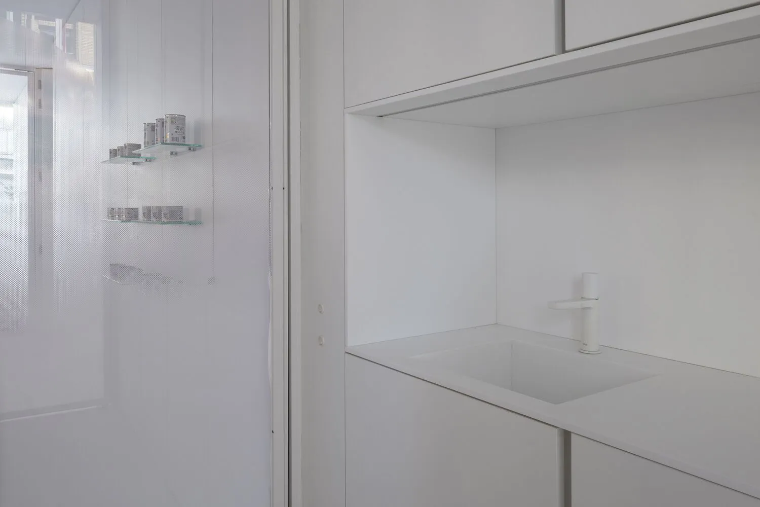 A minimalist white kitchen with white tiles, clean lines, and a white countertop.