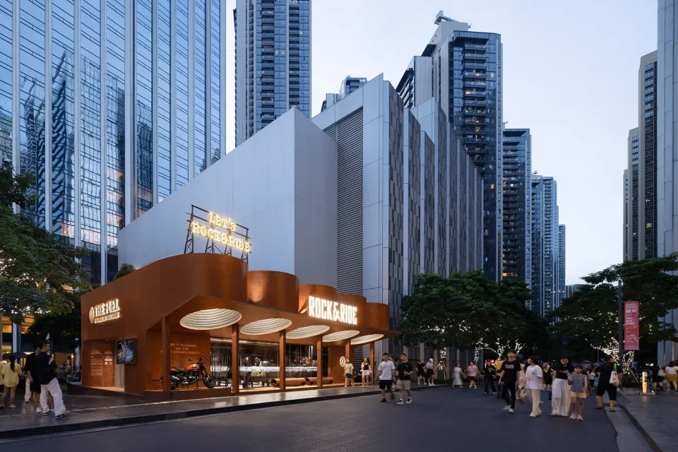 A modern, architecturally striking commercial building with a unique metal-clad façade and illuminated signage in a bustling