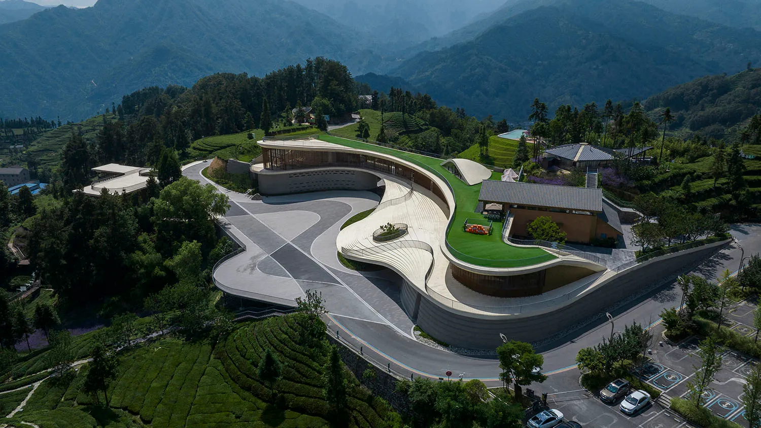 一座擁有混凝土外觀的現代建築,周圍環繞著茂密綠意與山景。