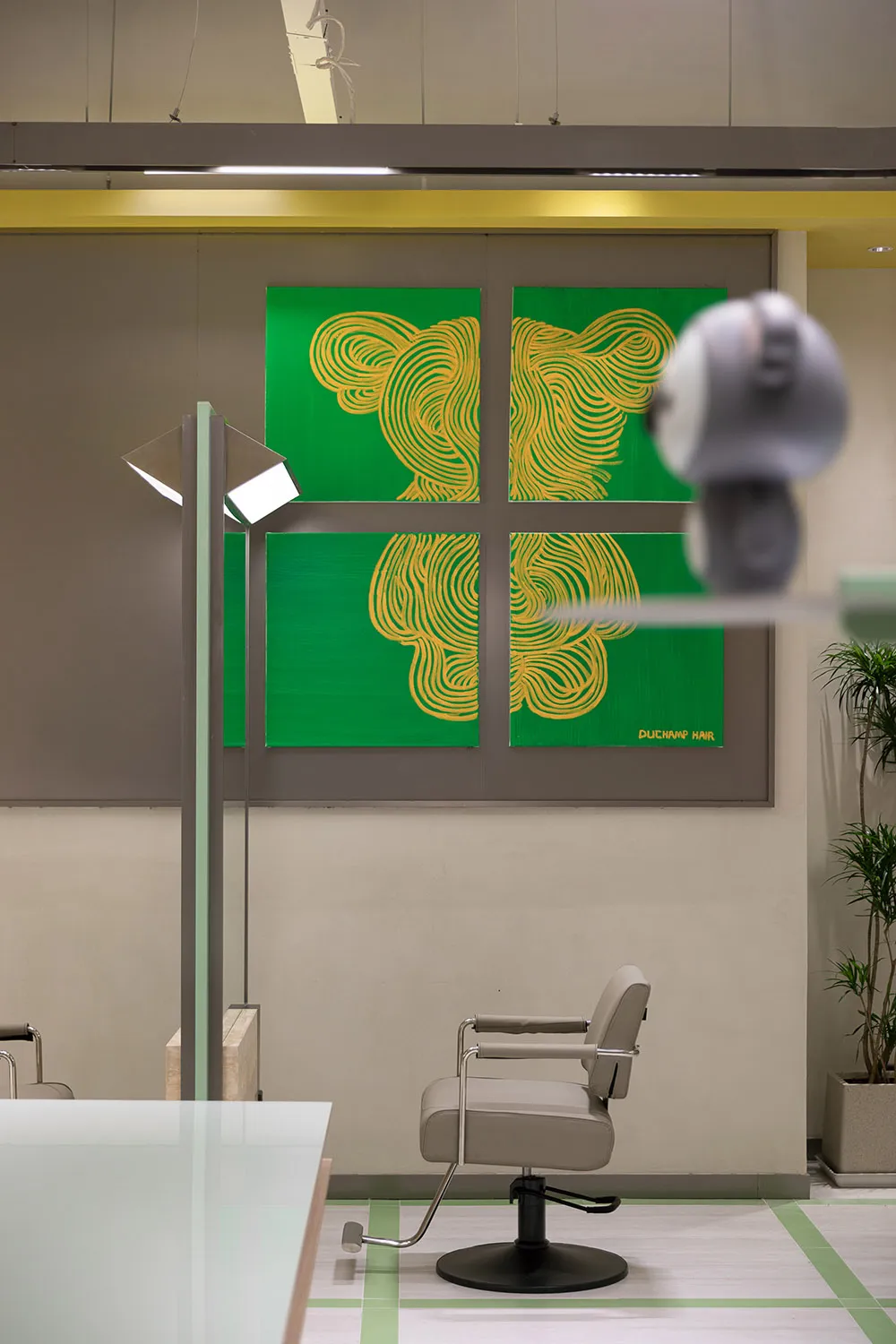 A modern hair salon interior featuring metallic furniture, green matte finish walls, and a decorative plant.