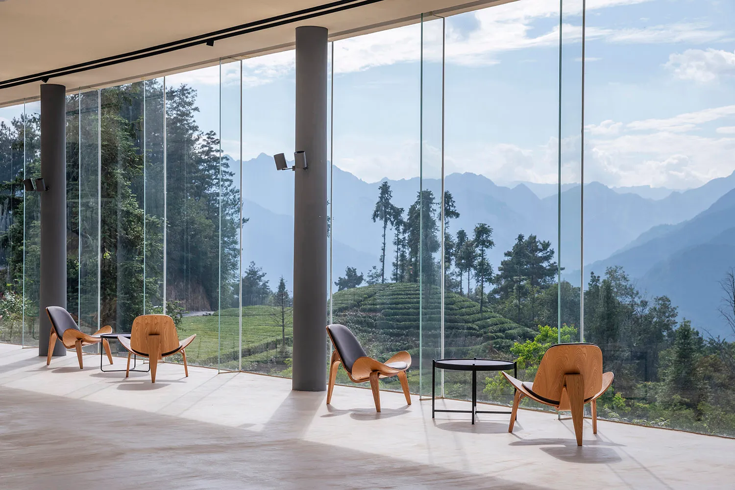 Modern minimalist living room featuring a white floor, large glass windows with a scenic mountain view, and three wooden armc