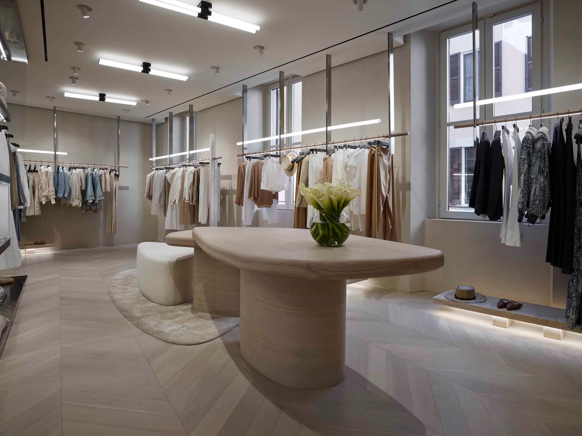 Modern retail store with clothing racks, a wooden central table, and a glass vase with flowers.
