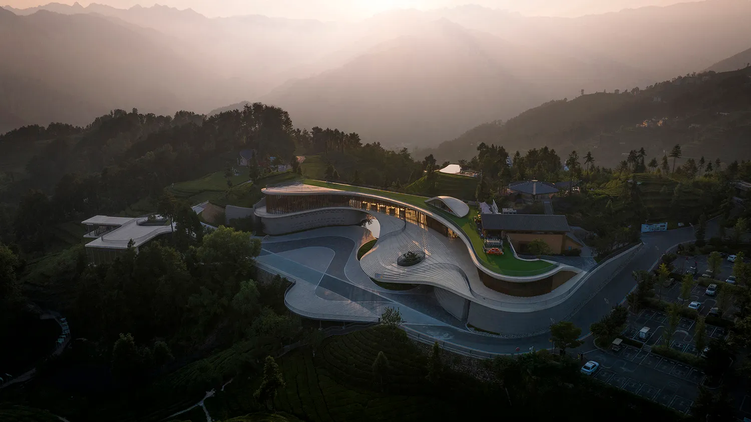 一座現代曲線混凝土建築，綠色屋頂映襯著山景。