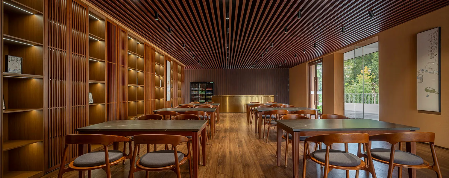 A spacious restaurant interior with wooden furniture and walls, a wooden slatted ceiling, and large windows.