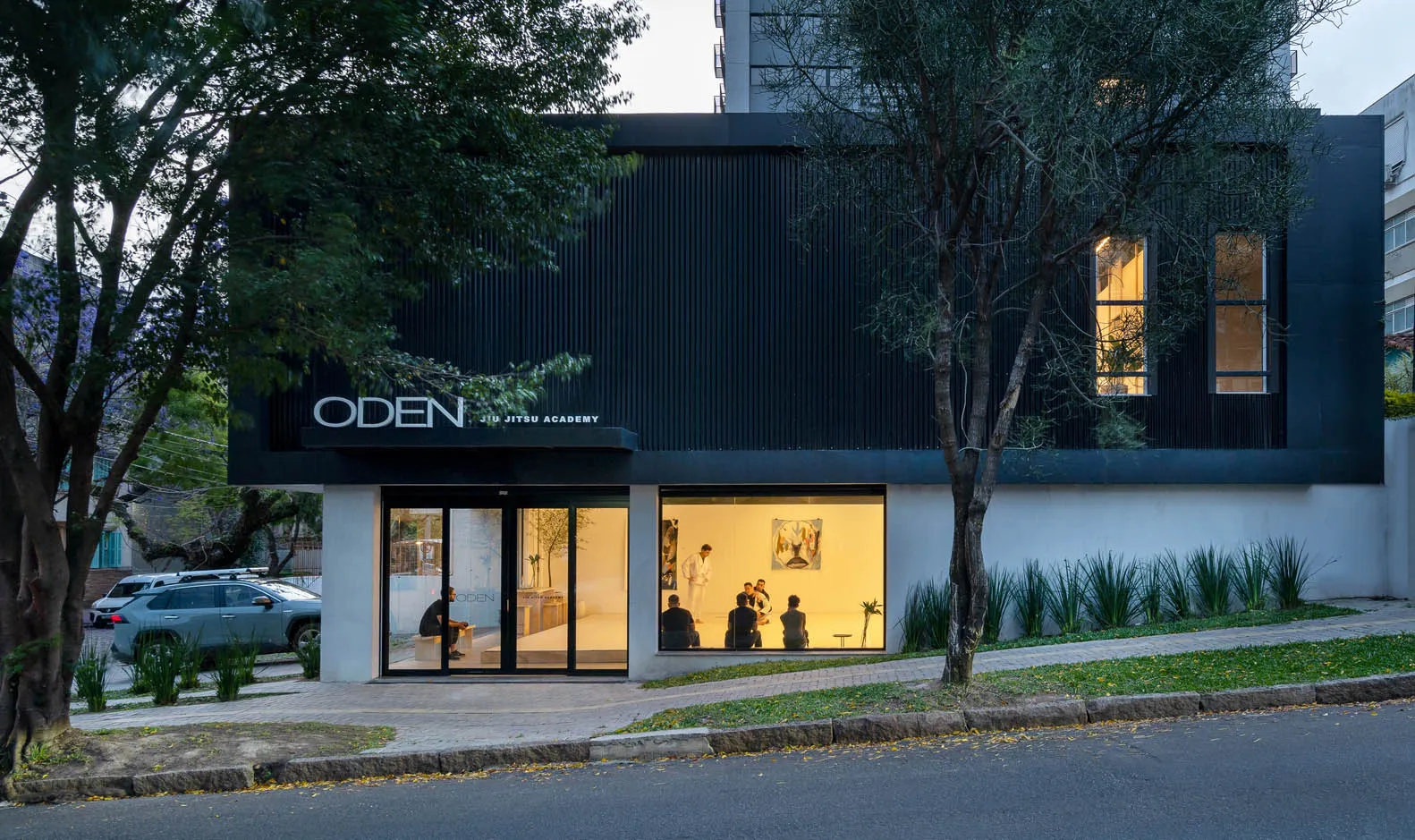 Modern metal-clad storefront for a jiu-jitsu academy with people practicing martial arts inside.