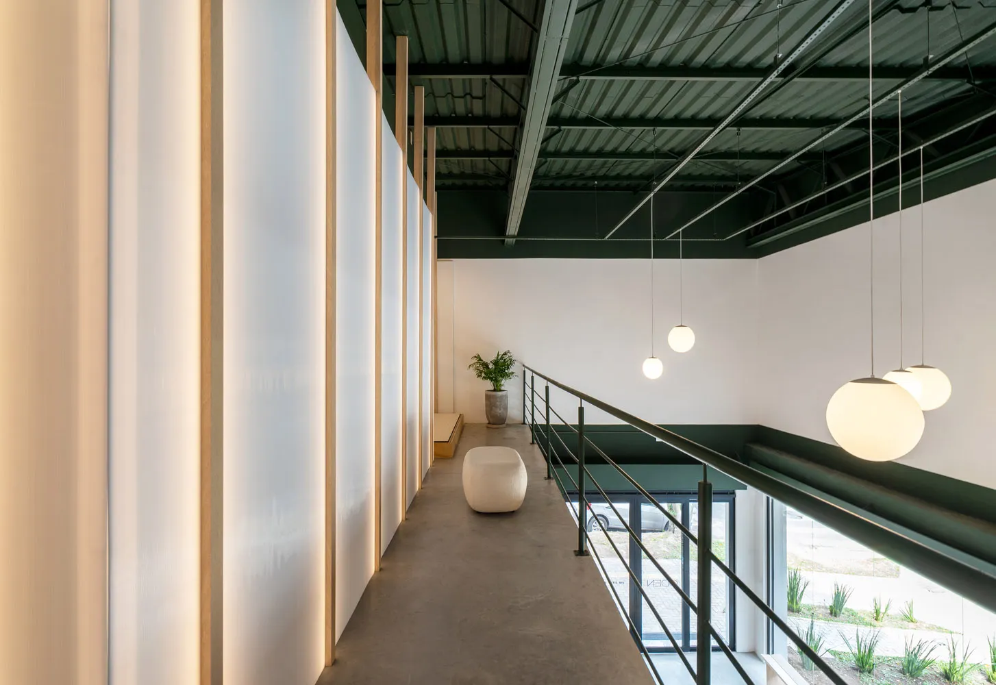 A modern industrial office space featuring concrete flooring and walls, with minimalistic furniture and hanging spherical lig
