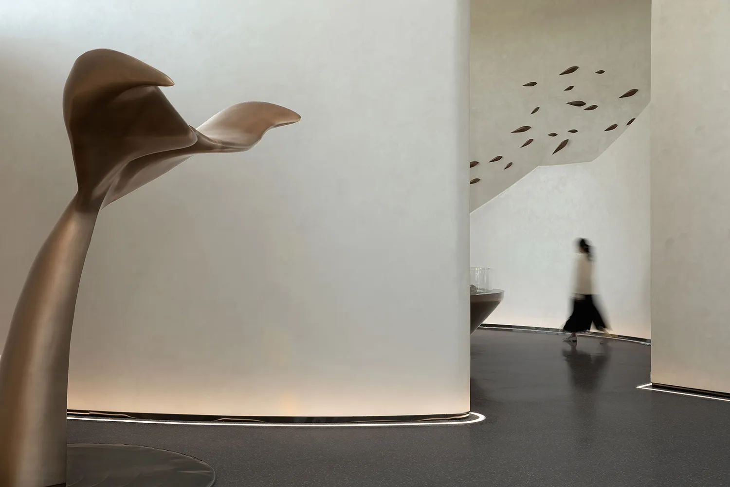 A minimalist interior space featuring concrete elements, with a blurred figure walking through the space.