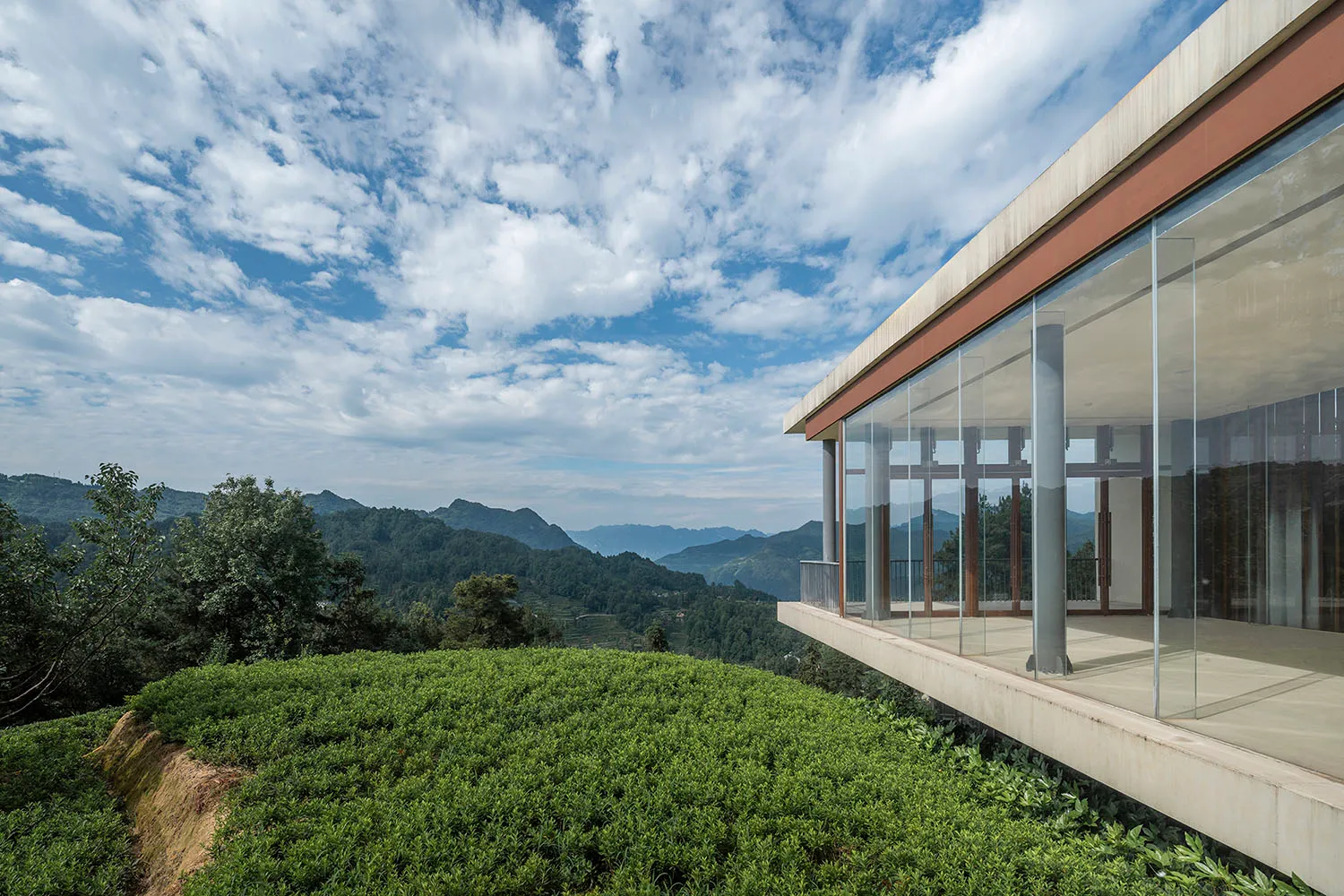 A modern residential terrace with glass walls overlooking green fields and mountains.