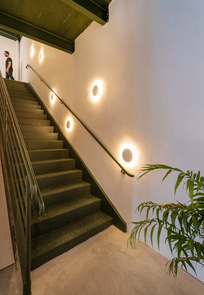 A minimalist staircase with metal steps and a metal railing against a white wall with round lights.