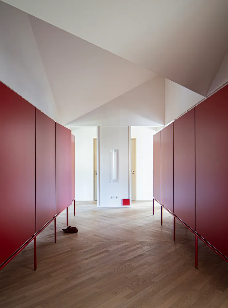 A minimalist hallway with red cabinets on either side and a light-colored wooden floor. There is a red object on the floor.