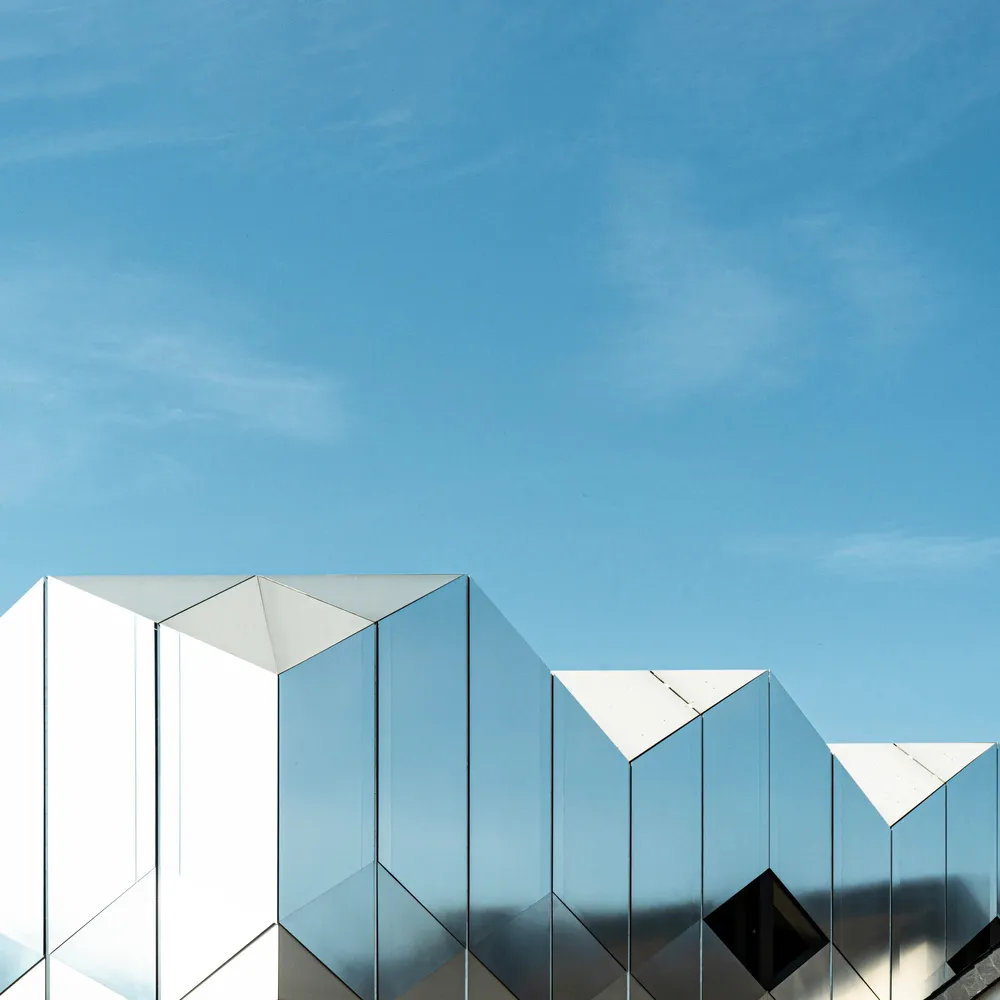 Modern building facade covered in reflective, mirrored glass panels against a clear blue sky.