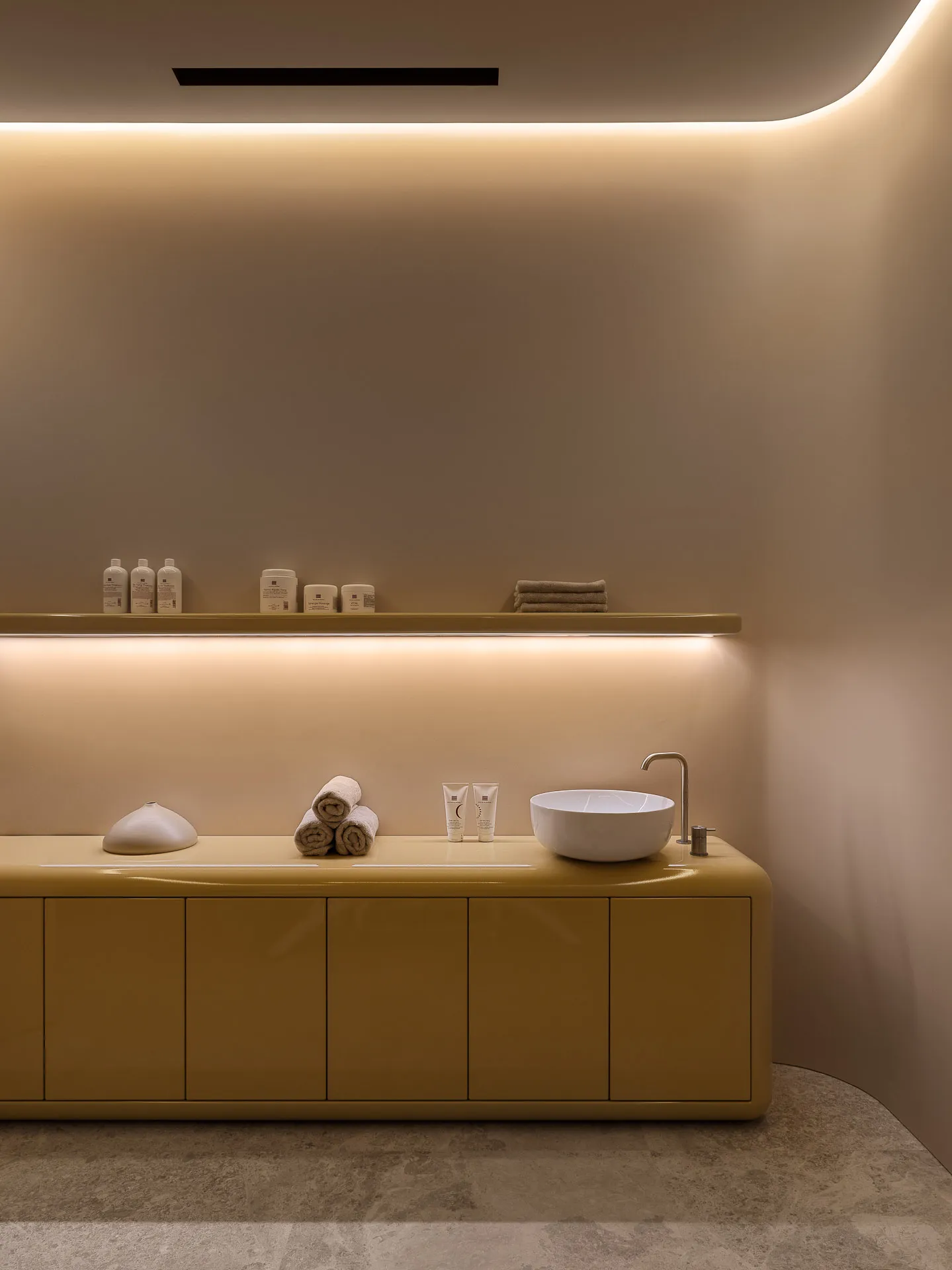A modern minimalist bathroom with a yellow cabinet, white sink, and beige marble floor.