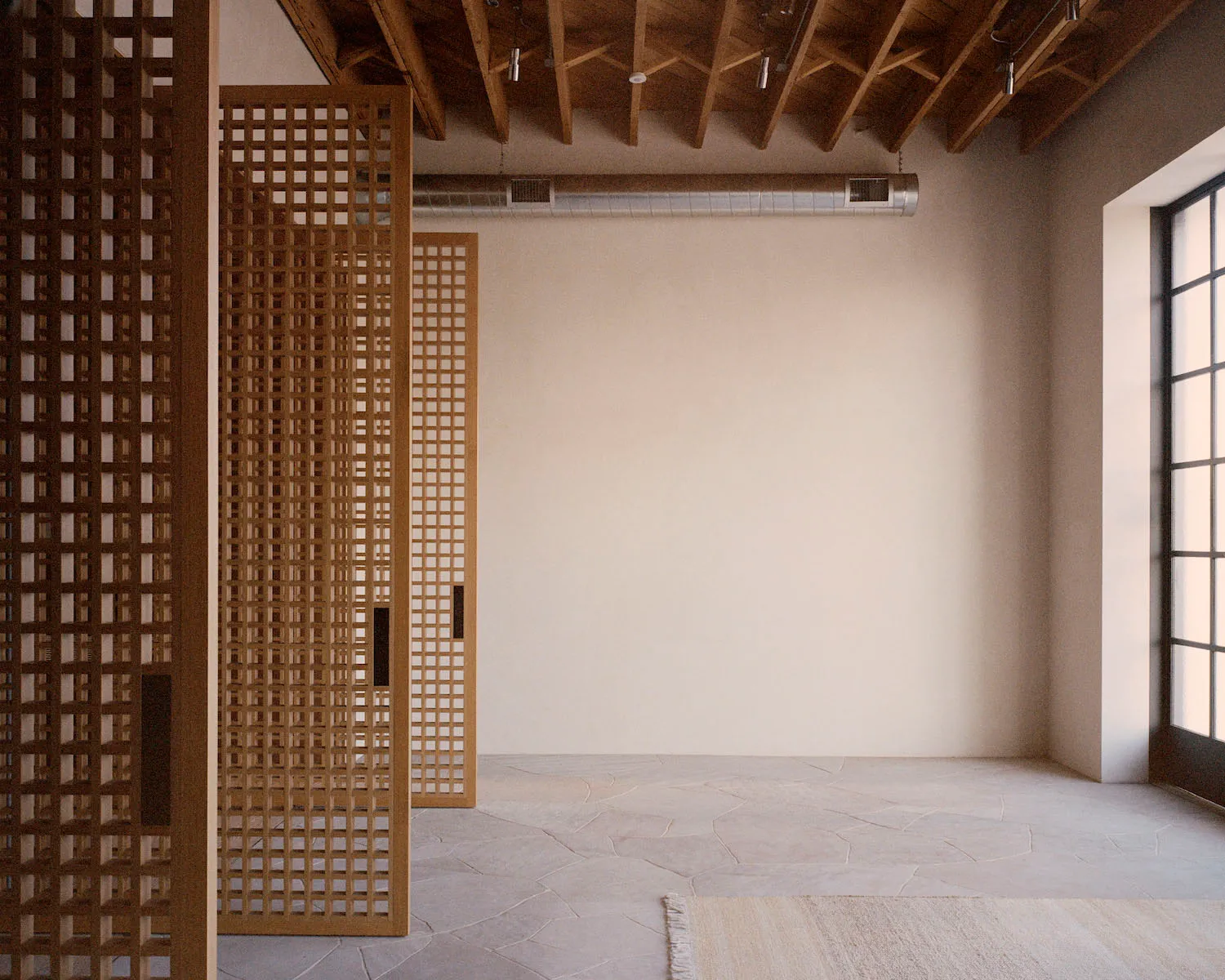 Minimalist room with concrete walls, wooden lattice screens, and exposed ceiling beams.