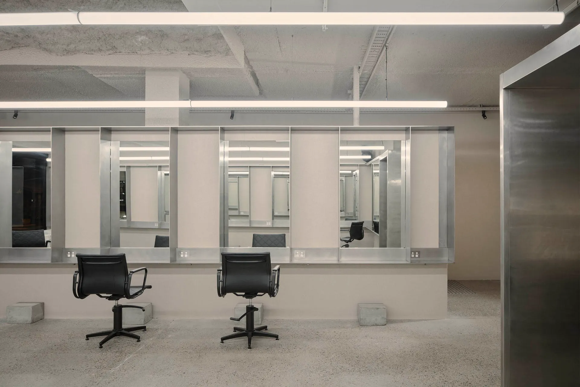 Minimalist interior design of a hair salon featuring concrete walls and mirrors.