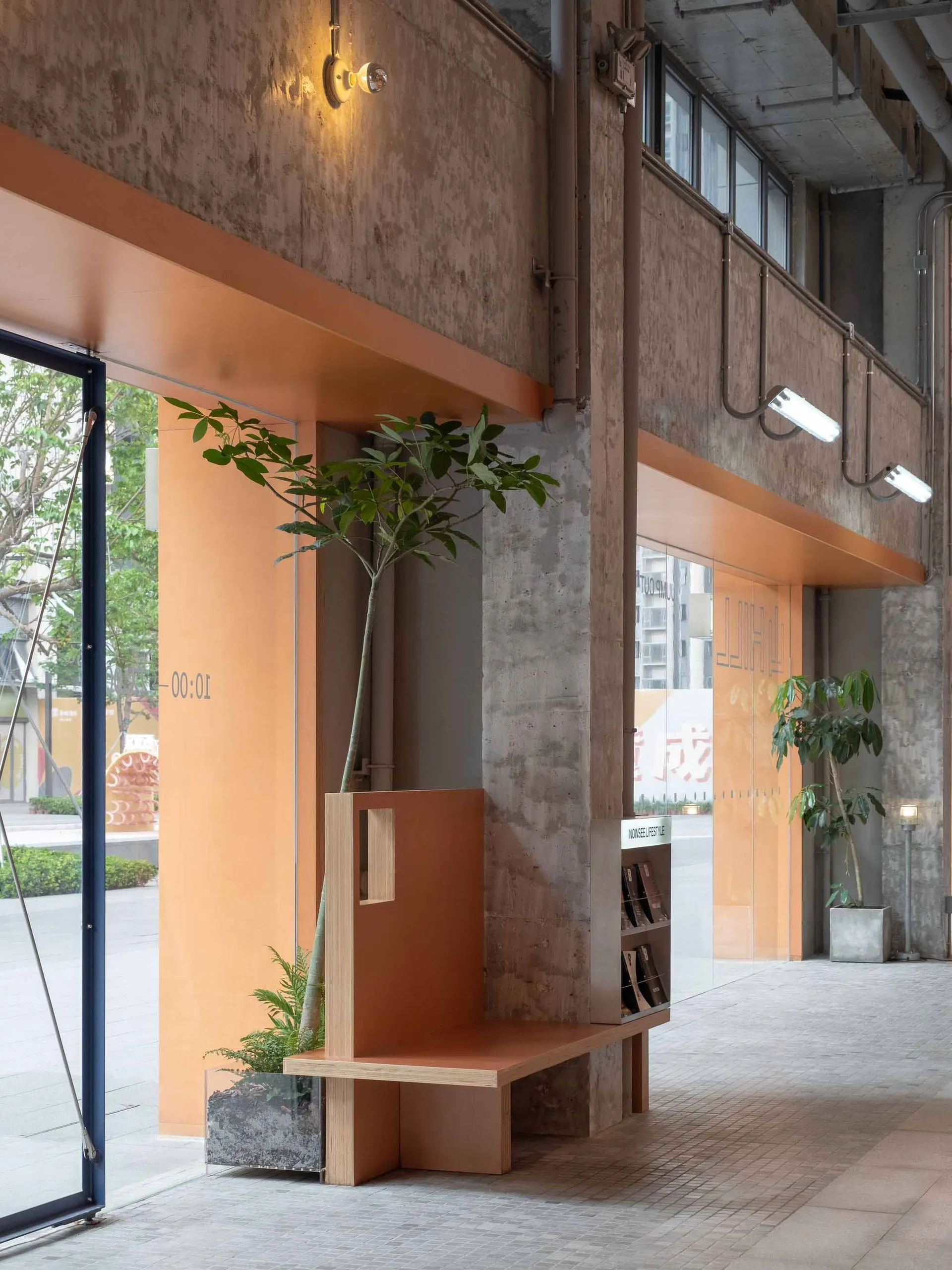 A cozy, industrial-style lobby with exposed concrete walls, plants, and warm lighting.