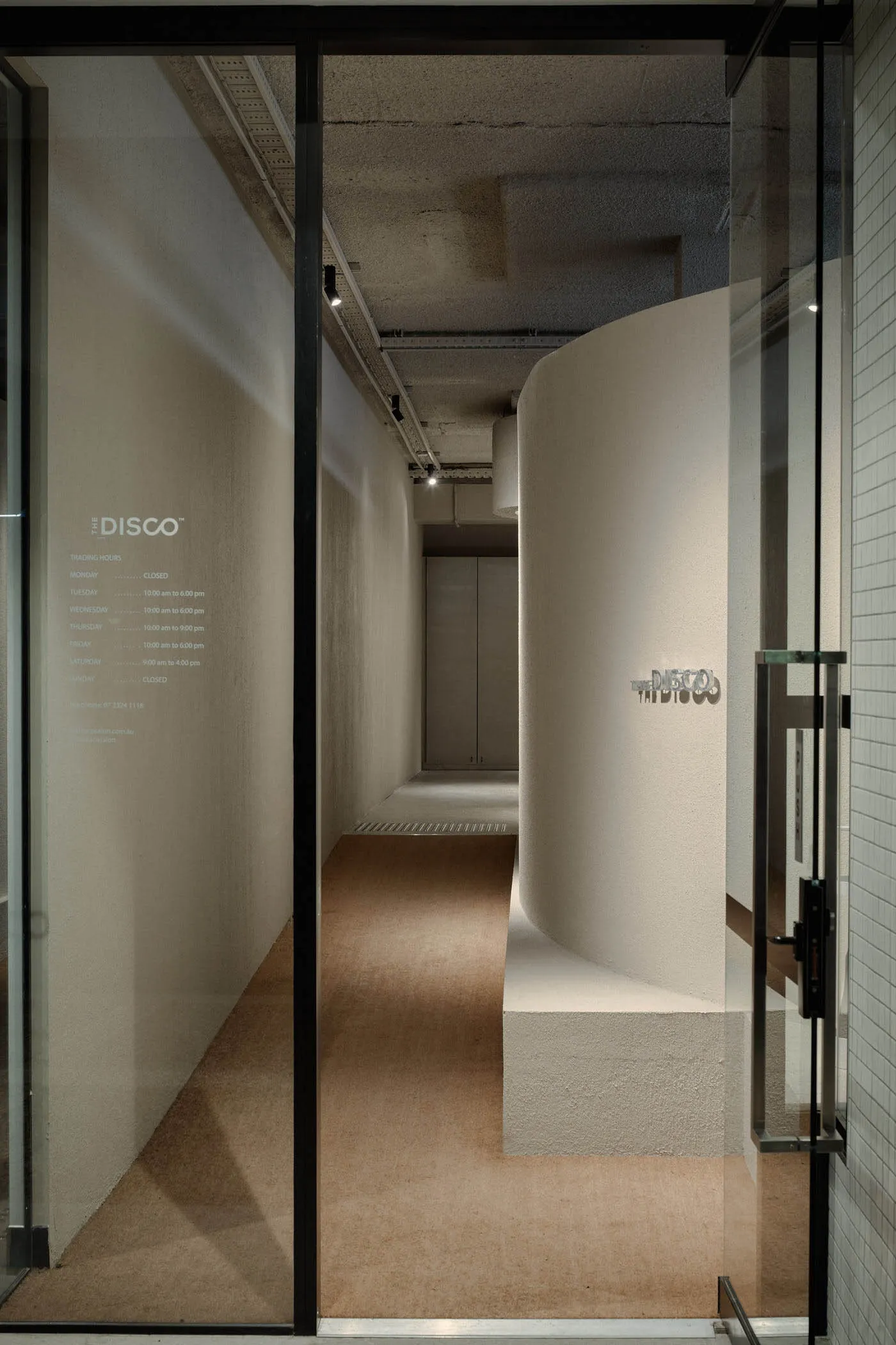 A modern office hallway with a concrete pathway lined by gray-colored walls and a reception desk.