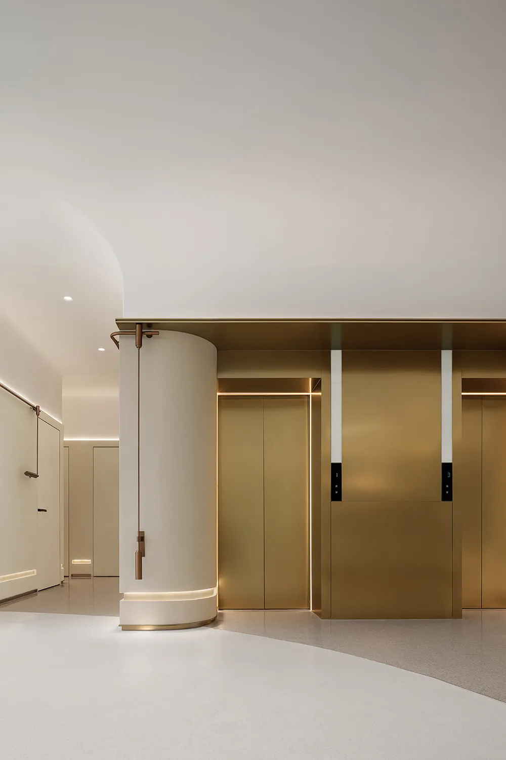 A modern minimalist hotel lobby featuring metallic brass finishes and a cylindrical column.